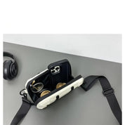 Borsa a tracolla bianca aperta su tavolo grigio, contenente smartphone e auricolari. Accessori moda, tecnologia, design moderno.