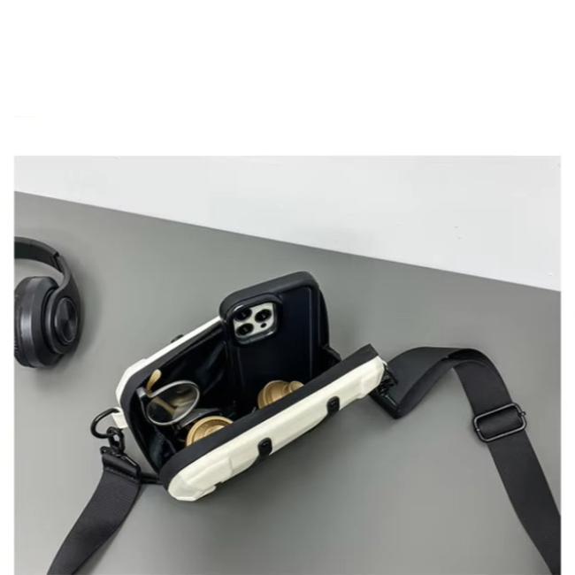 Borsa a tracolla bianca aperta su tavolo grigio, contenente smartphone e auricolari. Accessori moda, tecnologia, design moderno.