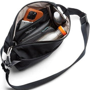 Borsa a tracolla nera aperta con tasche interne, contenente smartphone, bottiglia d'acqua e accessori. Design moderno e funzionale per viaggi.