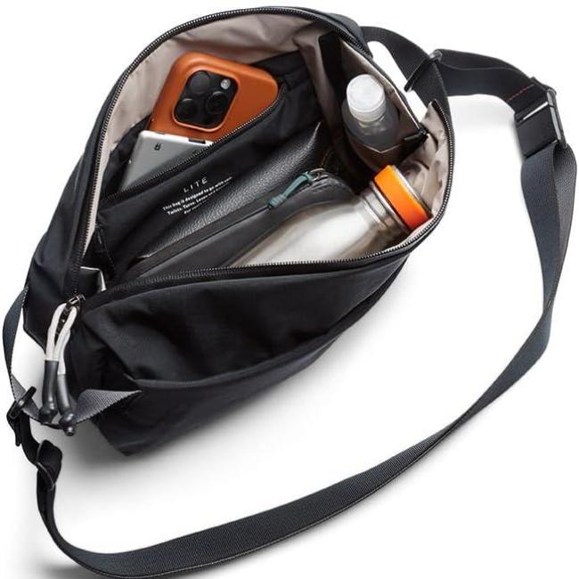 Borsa a tracolla nera aperta con tasche interne, contenente smartphone, bottiglia d'acqua e accessori. Design moderno e funzionale per viaggi.