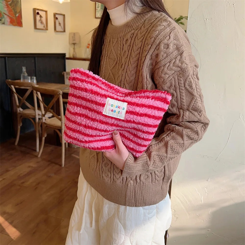 Donna con maglione marrone tiene borsa a righe rosa e rosse in pelliccia sintetica. Accessorio moda femminile, stile casual, tendenza autunno inverno.