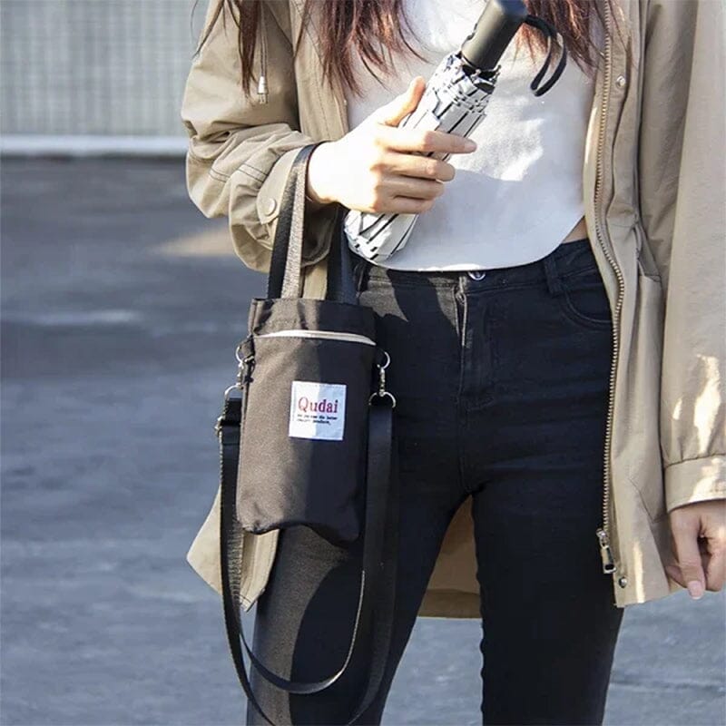 Donna con giacca beige e borsa nera a tracolla, tiene un ombrello pieghevole. Moda casual, accessori pratici, stile urbano.