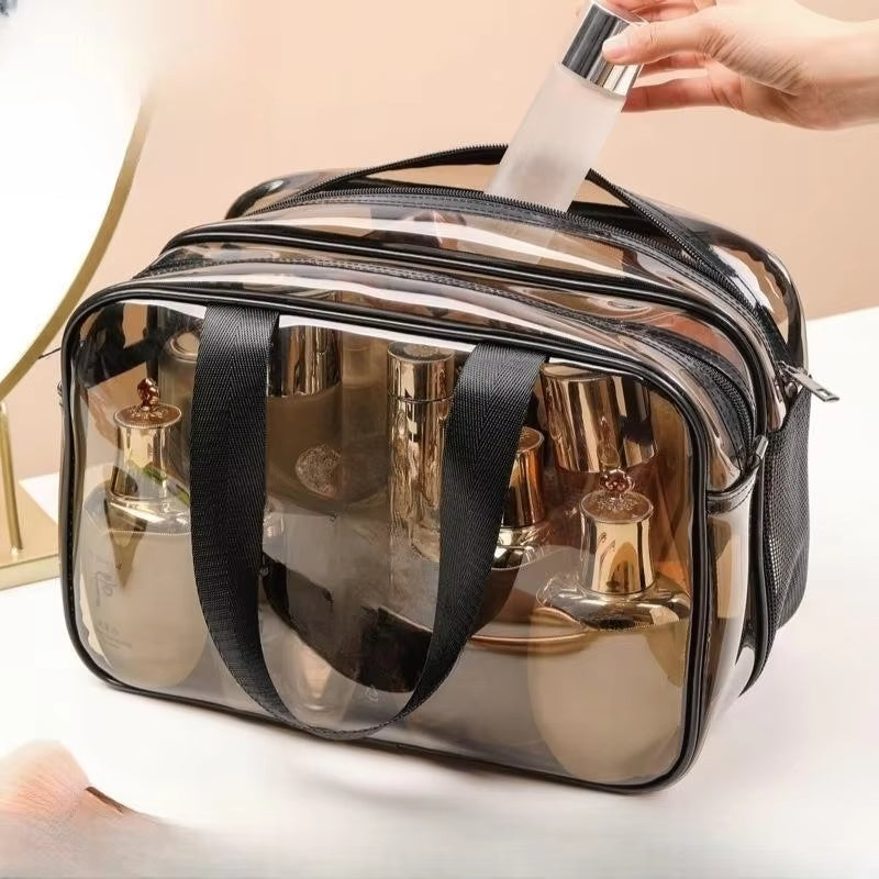 Borsa trasparente per cosmetici con manici neri, contenente flaconi di profumo e lozioni. Ideale per viaggi, organizzazione trucco, accessori beauty.