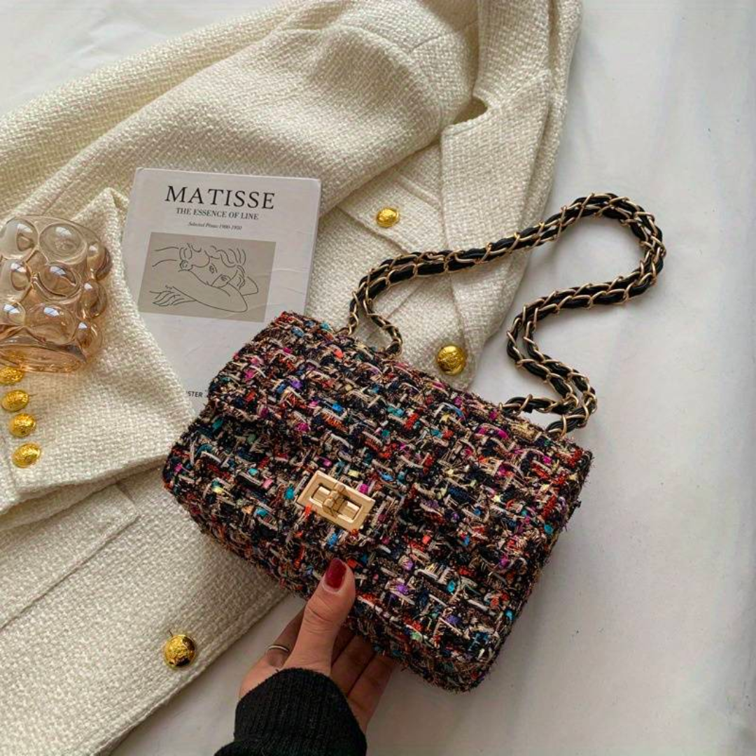 Borsa a tracolla in tweed multicolore su cappotto bianco, con catena dorata e chiusura a scatto. Accessorio moda elegante e chic.