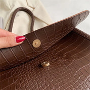 Borsa in pelle marrone con texture coccodrillo, chiusura a bottone magnetico, dettaglio elegante, moda donna, accessorio di lusso.