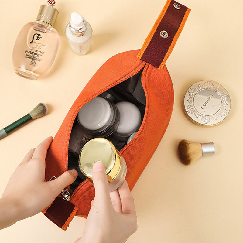 Borsa cosmetica arancione aperta con prodotti di bellezza, pennelli trucco e flaconi su sfondo beige. Accessori make-up, organizzazione viaggio.
