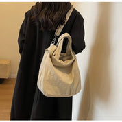 Donna con cappotto nero indossa borsa a tracolla beige in tessuto, design casual e moderno, ideale per moda autunno inverno.