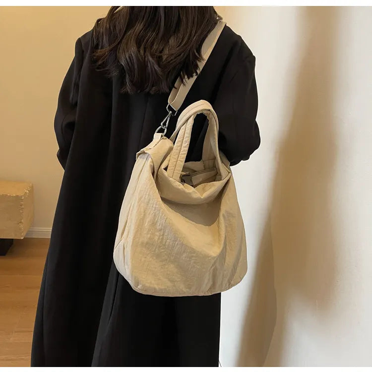 Donna con cappotto nero indossa borsa a tracolla beige in tessuto, design casual e moderno, ideale per moda autunno inverno.