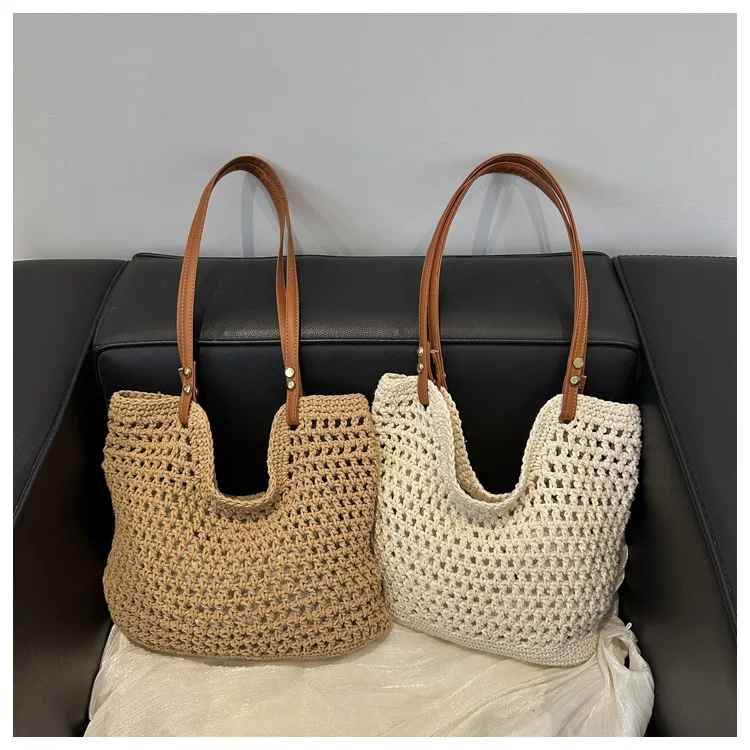 Due borse a maglia in paglia beige e bianca con manici in pelle marrone su divano nero. Eleganti, estive, perfette per lo shopping o la spiaggia.