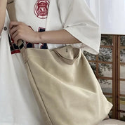 Utente con borsa a tracolla beige in tela, indossa maglietta bianca con stampa. Accessorio casual, moda urbana, stile quotidiano.
