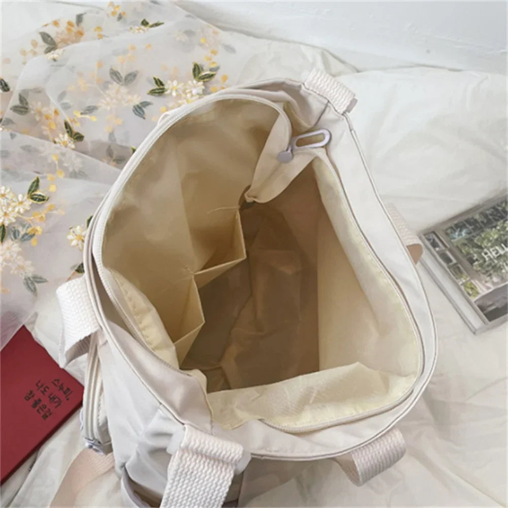 Borsa a tracolla beige aperta, con tasche interne, su letto con coperta floreale. Accessorio moda donna, capiente e versatile per uso quotidiano.