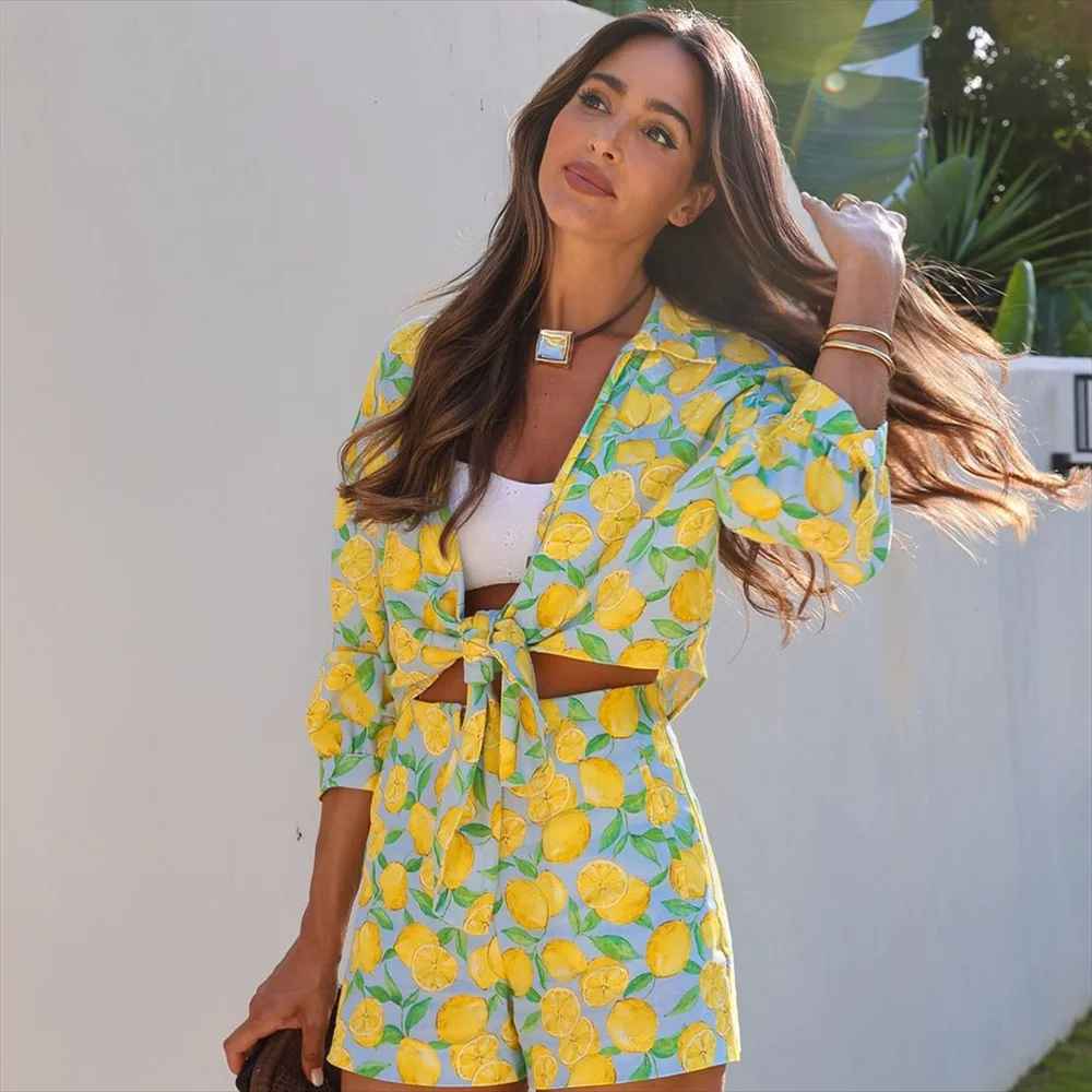 Donna con completo estivo a fantasia limoni, top annodato e shorts coordinati, sfondo esterno. Moda estiva, abbigliamento casual, stile fresco.