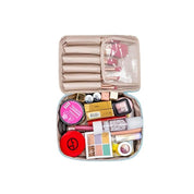 Borsa trucco da viaggio aperta, beige, con scomparti organizzati contenenti cosmetici vari, pennelli e accessori per il make-up.