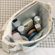 Borsa a tracolla bianca con motivo floreale, contenente tablet, smartphone, cosmetici e accessori. Ideale per organizzazione e stile quotidiano.
