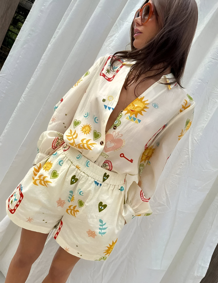 Donna con camicia e pantaloncini coordinati a fantasia colorata, sfondo bianco. Abbigliamento estivo, moda femminile, stile casual.