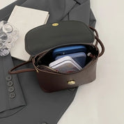 Borsa a tracolla in pelle marrone aperta su giacca grigia, contenente smartphone blu e custodia trasparente. Elegante accessorio moda donna.
