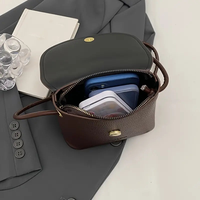Borsa a tracolla in pelle marrone aperta su giacca grigia, contenente smartphone blu e custodia trasparente. Elegante accessorio moda donna.