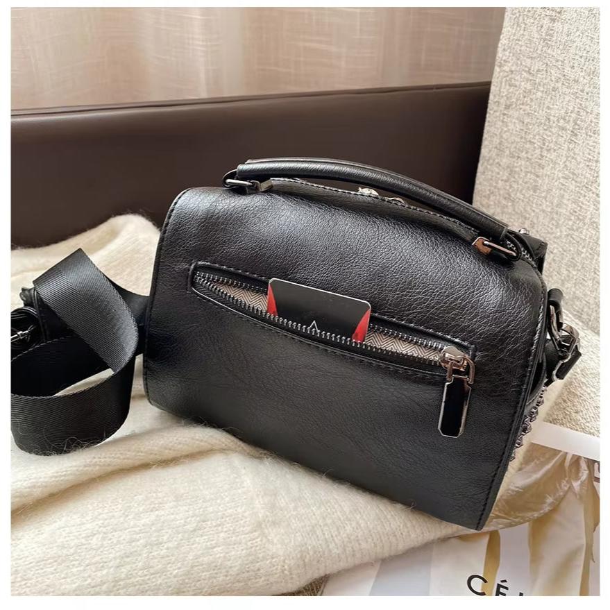 Borsa a tracolla in pelle nera su divano, con tasca frontale con zip e manico superiore. Design elegante, ideale per moda donna e accessori.