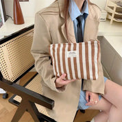 Donna con giacca beige tiene una pochette a righe marroni e bianche. Moda autunnale, accessori eleganti, stile casual chic.