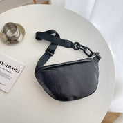 Marsupio nero in pelle su tavolo bianco, con tazza di caffè e rivista. Accessorio moda unisex, stile casual, ideale per viaggi e uso quotidiano.