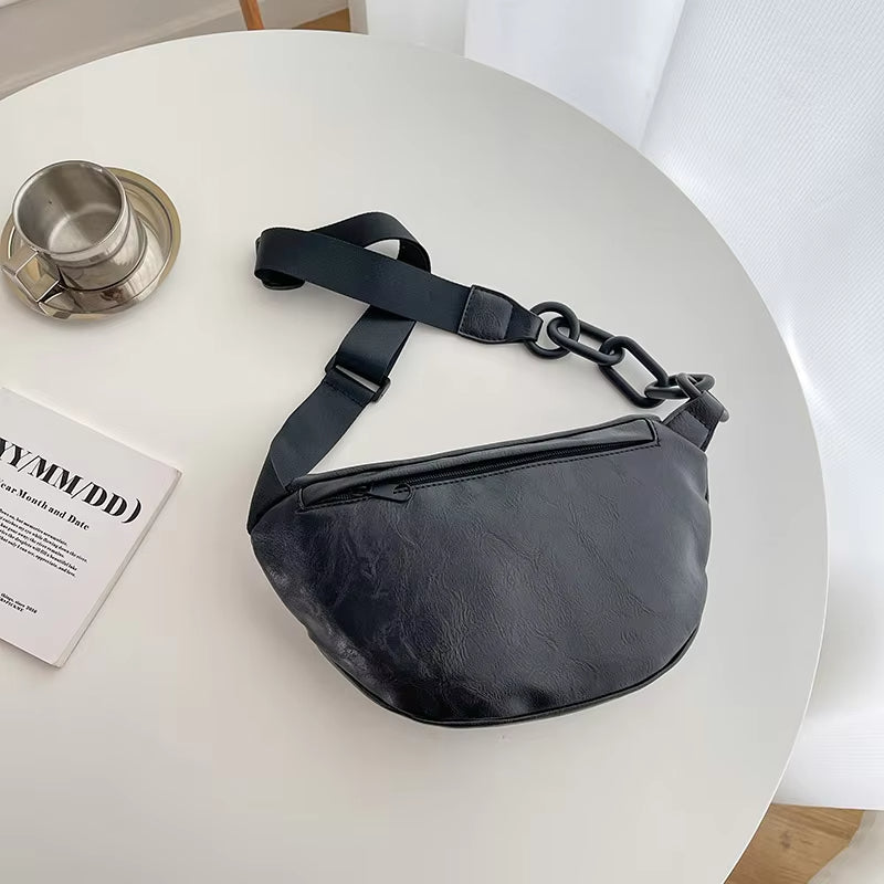 Marsupio nero in pelle su tavolo bianco, con tazza di caffè e rivista. Accessorio moda unisex, stile casual, ideale per viaggi e uso quotidiano.