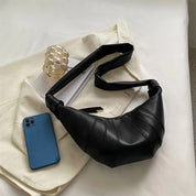 Borsa a spalla nera in pelle su tavolo bianco, accanto a smartphone blu e decorazione in vetro. Accessorio moda elegante e moderno.