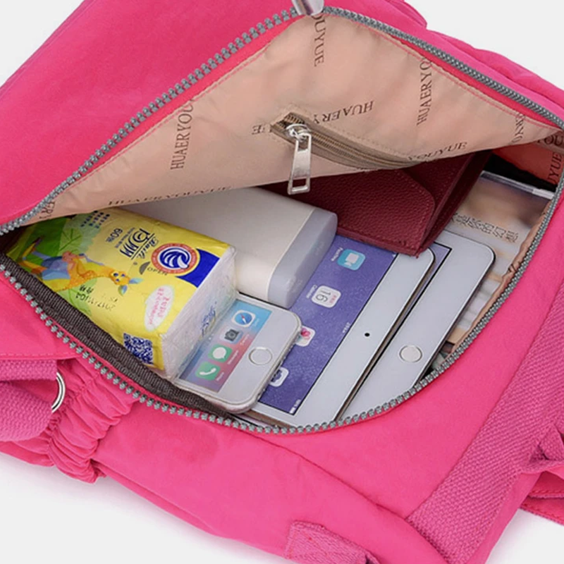 Zaino rosa aperto con tablet, smartphone, power bank e fazzoletti all'interno. Accessori tecnologici e pratici per il viaggio.