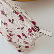 Astuccio in tessuto floreale con cerniera, motivo rose rosse su sfondo beige. Accessorio moda elegante, ideale per cosmetici o piccoli oggetti.