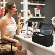 Donna che applica rossetto davanti a uno specchio, accanto a una borsa trucco nera su un tavolo da toeletta. Accessori cosmetici e specchio visibili.