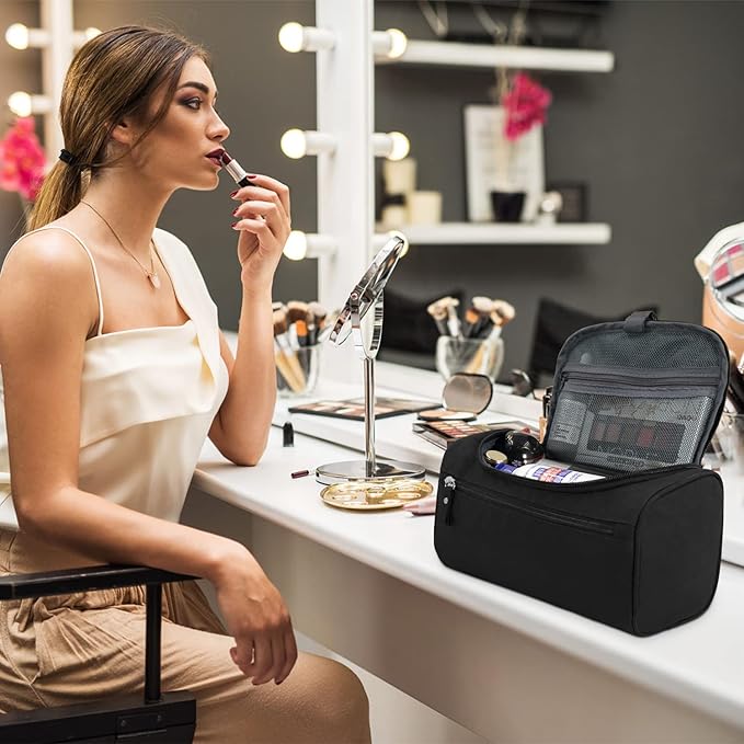 Donna che applica rossetto davanti a uno specchio, accanto a una borsa trucco nera su un tavolo da toeletta. Accessori cosmetici e specchio visibili.