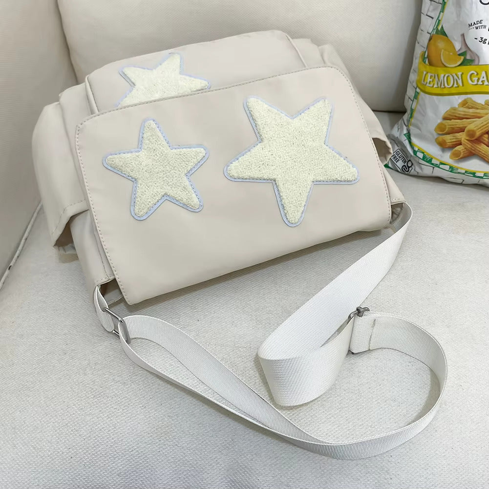 Borsa a tracolla beige con stelle bianche in rilievo, design moderno, su divano bianco. Accanto, confezione di snack al limone.