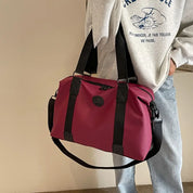 Borsa a tracolla unisex in tessuto rosso con manici neri, indossata da persona in felpa grigia e jeans. Accessorio moda casual e versatile.