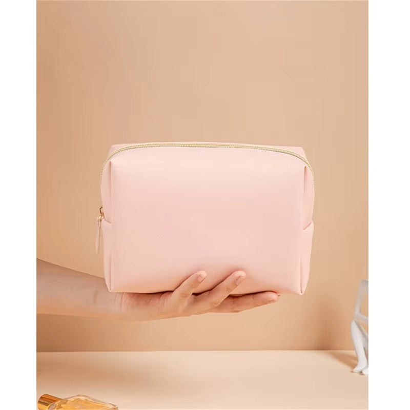 Borsa cosmetica rosa chiaro in pelle sintetica, chiusura con cerniera dorata, design elegante e compatto, ideale per viaggi e organizzazione trucco.