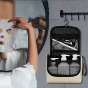 Borsa da viaggio appesa con flaconi cosmetici, accanto a specchio con persona che applica maschera viso. Organizzazione bagno, cura della pelle.