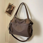 Borsa a tracolla marrone in pelle sintetica, design elegante, con manici e cerniere, appesa a un gancio su parete bianca. Accessorio moda donna.