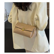 Borsa a tracolla beige in pelle, design elegante, chiusura dorata, indossata su giacca bianca. Accessorio moda donna, stile sofisticato.