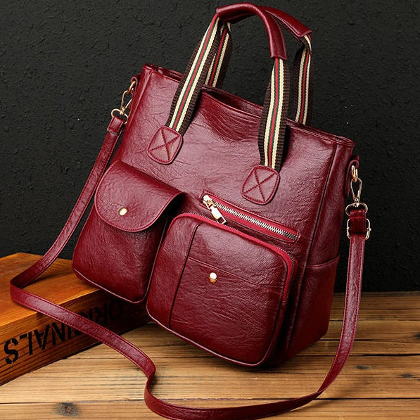Borsa a tracolla in pelle rossa con tasche frontali, manici a righe, e tracolla regolabile. Design elegante, ideale per moda donna e accessori.