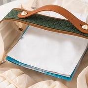 Borsa beige aperta con manico in pelle marrone e cerniera verde, contenente documenti e fogli bianchi. Accessorio moda elegante e funzionale.