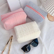 Tre astucci in tessuto trapuntato rosa, grigio e bianco su sfondo bianco, con occhiali da sole e ventaglio. Accessori moda eleganti e pratici.