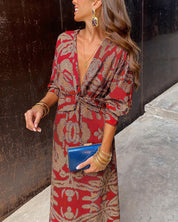 Donna con abito lungo rosso a fantasia, clutch blu, orecchini pendenti e bracciali dorati. Moda elegante, abbigliamento femminile, accessori chic.