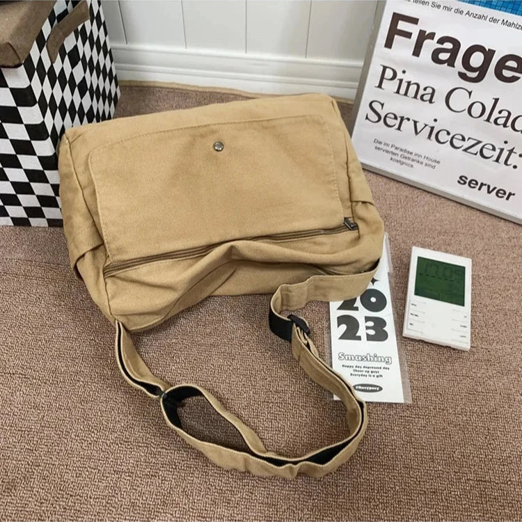 Borsa a tracolla beige su tappeto marrone, accanto a calendario 2023 e termometro digitale. Design casual, ideale per uso quotidiano.