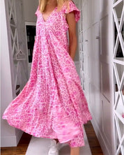 Abito lungo rosa con stampa leopardata, maniche corte, scollo a V, indossato da donna in corridoio. Moda estiva, abbigliamento casual elegante.