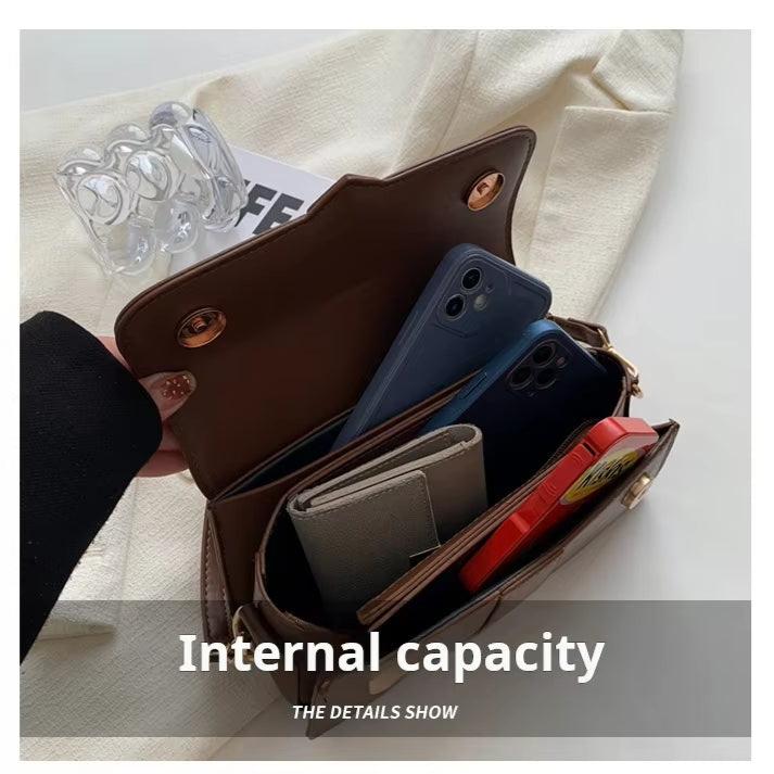 Borsa a tracolla marrone aperta con smartphone, portafoglio e accessori all'interno. Design compatto, ideale per organizzazione e moda quotidiana.