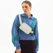 Donna con maglione blu-verde a rombi, indossa una borsa a tracolla bianca. Moda autunnale, accessori eleganti, stile casual chic.