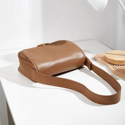 Borsa a tracolla in pelle marrone su tavolo bianco, design elegante e minimalista, perfetta per moda donna, accessorio versatile e chic.