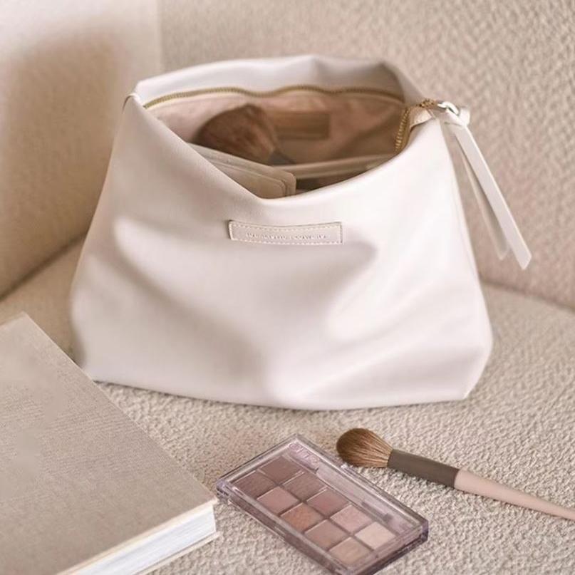 Borsa trucco bianca su sedia beige con pennelli e palette ombretti. Accessori cosmetici eleganti, ideale per organizzare il make-up.