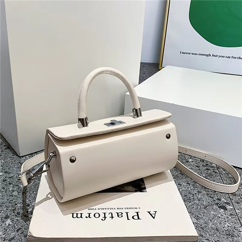 Borsa a mano in pelle bianca con tracolla regolabile, design elegante e moderno, posizionata su un libro, ideale per moda femminile e shopping.