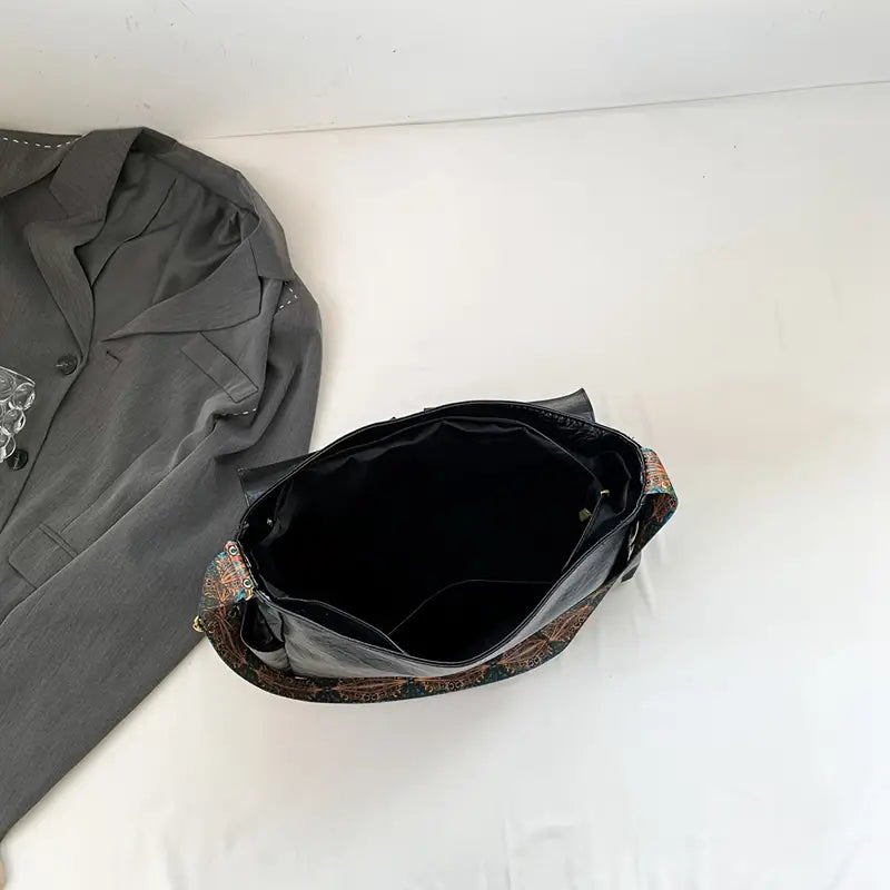Borsa a tracolla nera in pelle con interno spazioso, accanto a giacca grigia su sfondo bianco. Accessorio moda elegante e versatile.
