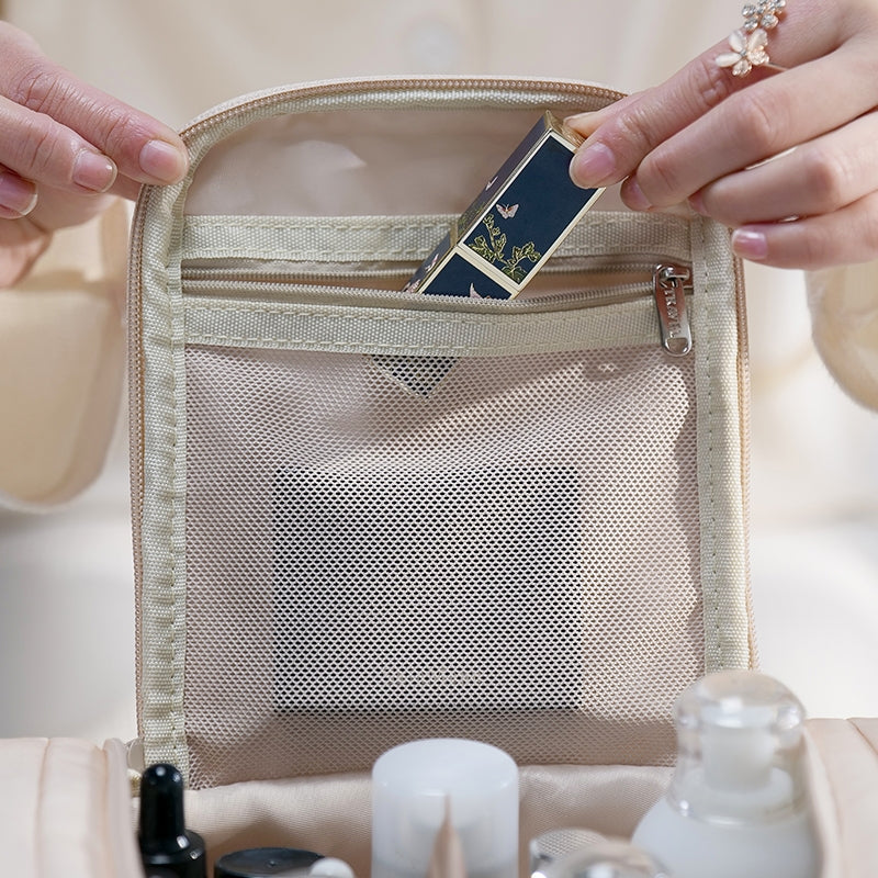 Mani femminili inseriscono un rossetto elegante in una borsa cosmetica beige con tasca a rete. Accessori trucco, organizzazione viaggio, bellezza.