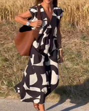 Abito lungo estivo nero e bianco con motivo astratto, indossato da una donna in un campo di grano. Accessori: borsa marrone, bracciale bianco.